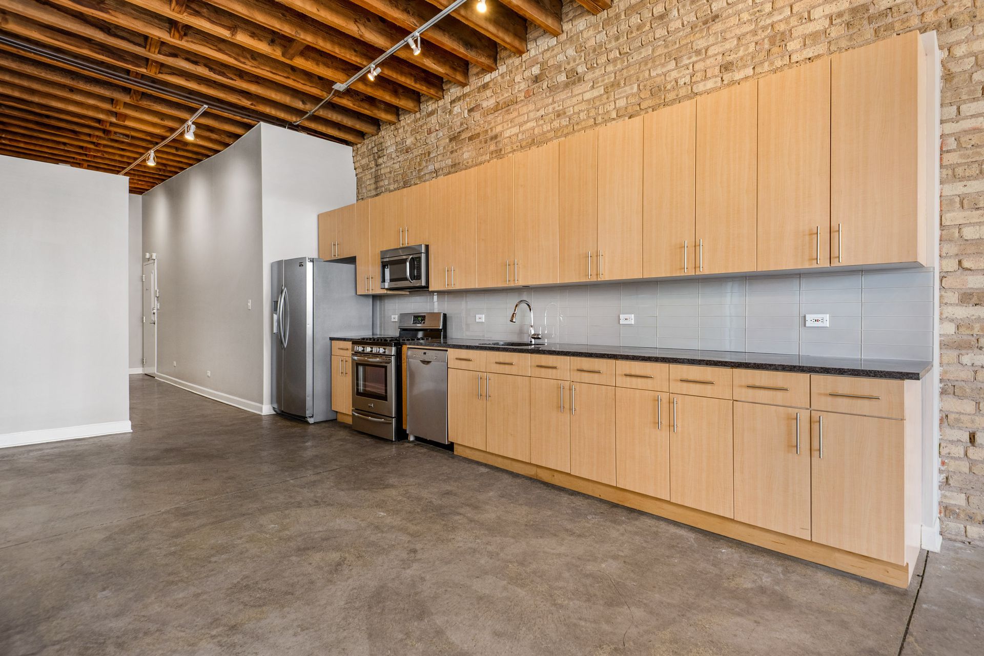 Spacious kitchen with wooden cabinets, stainless steel appliances, and a brick wall at 945 W Fulton Market Apartments.