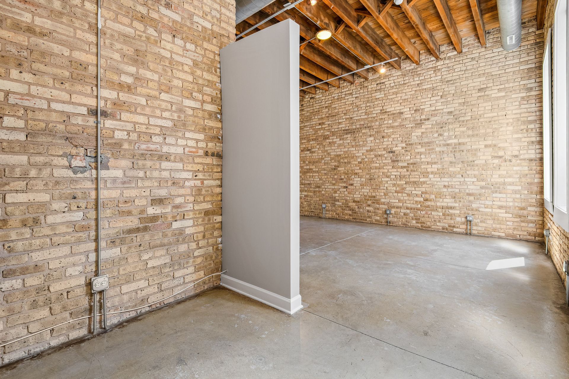 An empty apartment living room with a brick wall and a concrete floor.