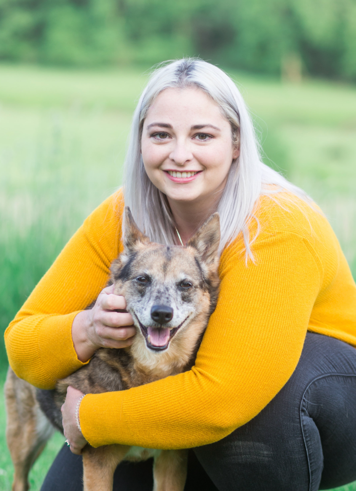 dr. jessi turner in a yellow sweater is kneeling down and holding a dog .