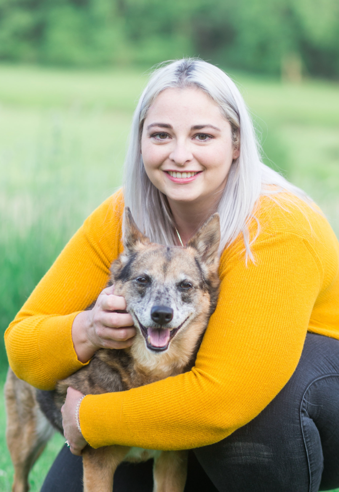 Dr. Jessi Turner in a yellow sweater is kneeling down and hugging a dog .