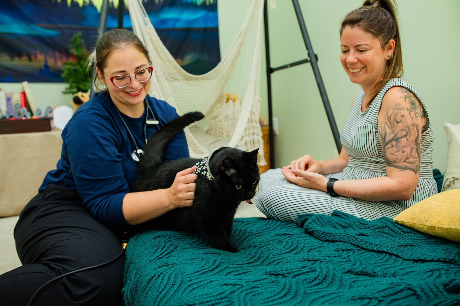 two women are sitting on a bed with a black cat .