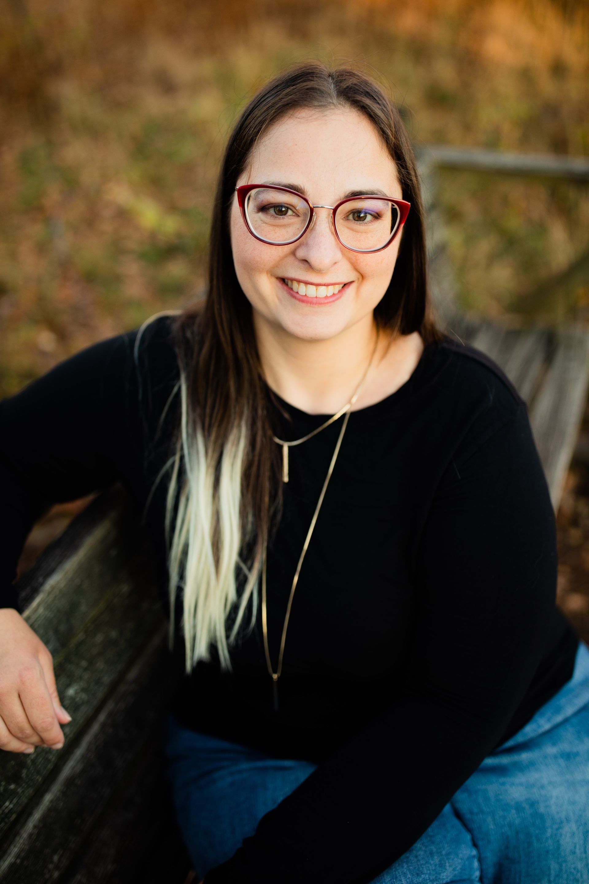 a woman wearing glasses and a black shirt is sitting on a bench .