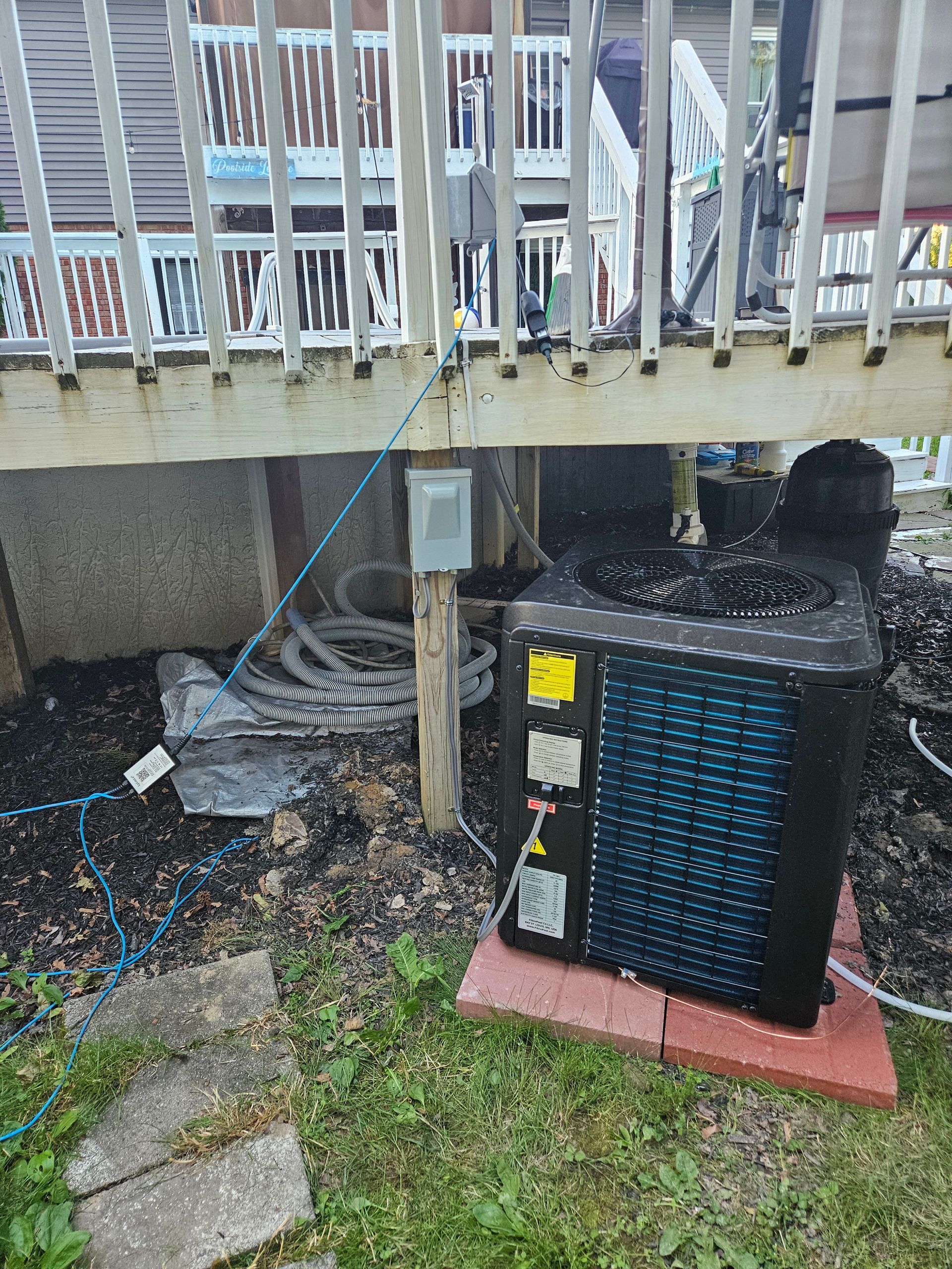 An air conditioner is sitting under a deck next to a house.