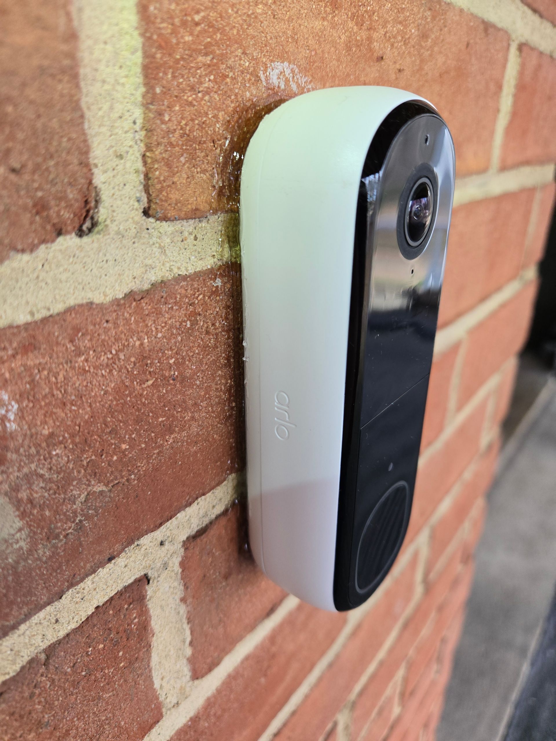 A white doorbell is attached to a brick wall.
