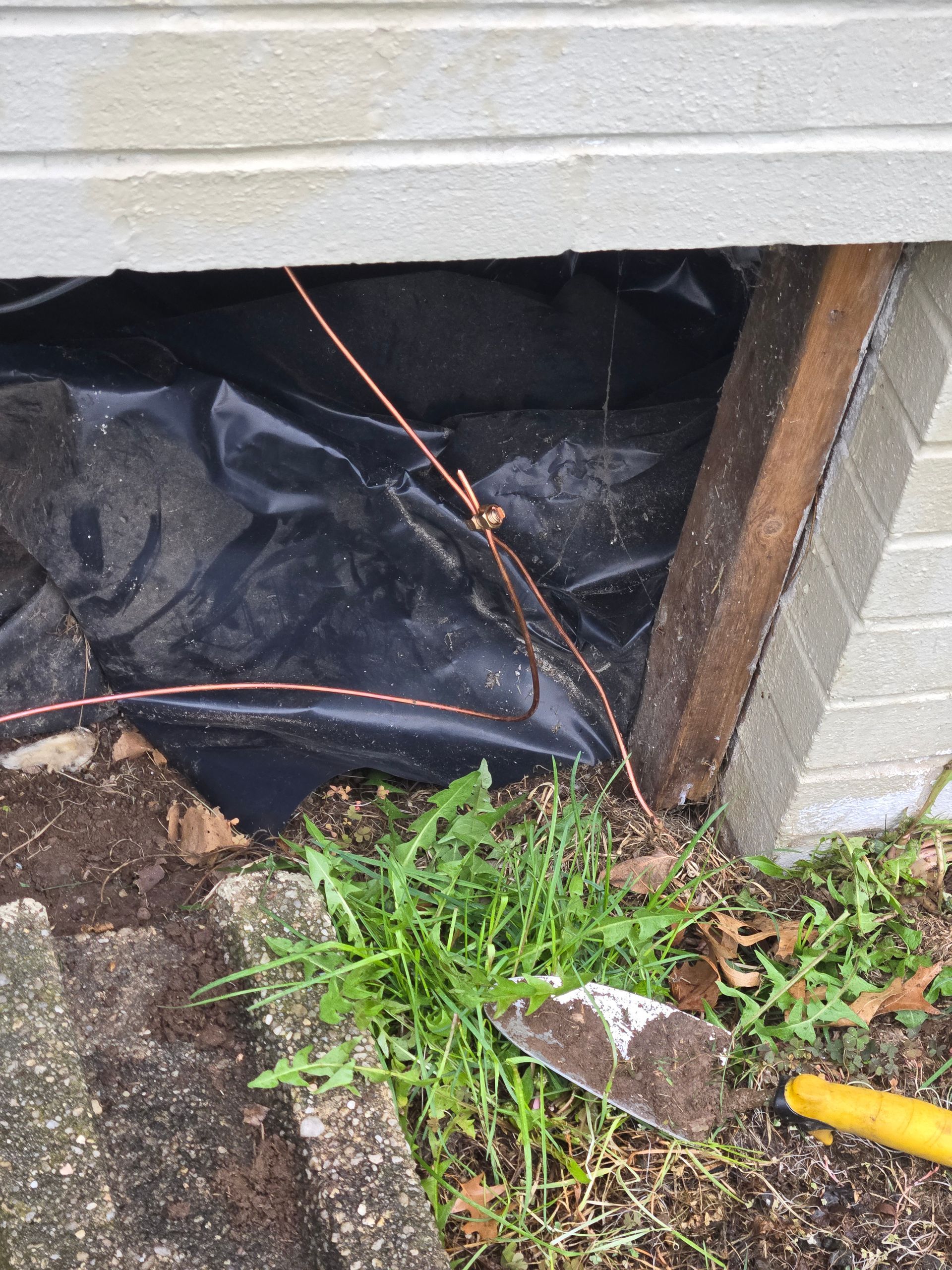 A shovel is laying on the ground next to a brick wall.