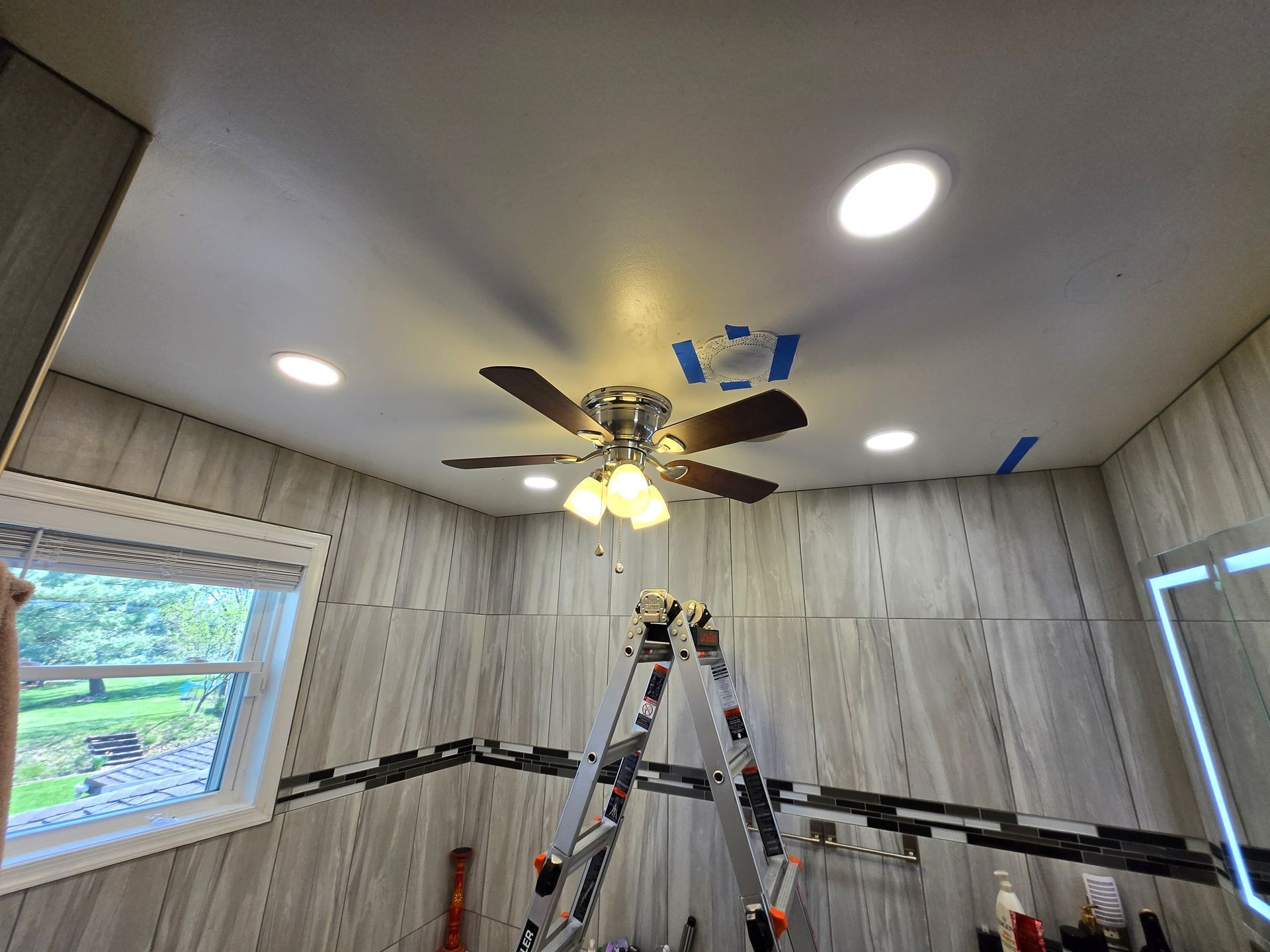 A bathroom with a ceiling fan and a ladder.