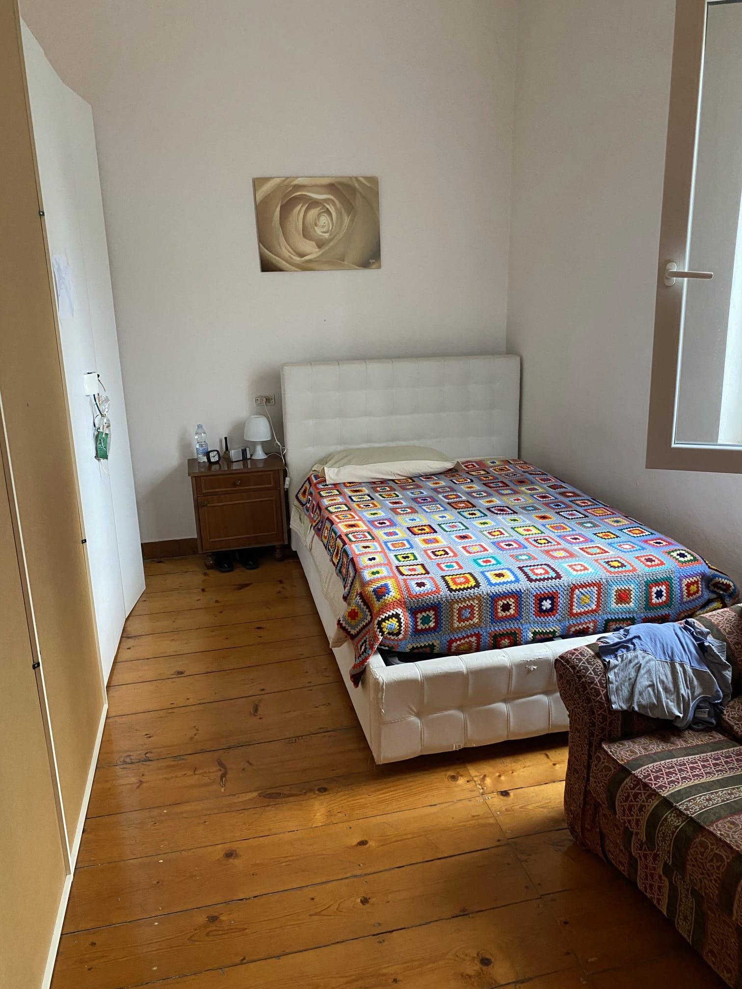 Camera da letto con letto, comodino e armadio su pavimento in legno. Una coperta a fantasia copre il letto.