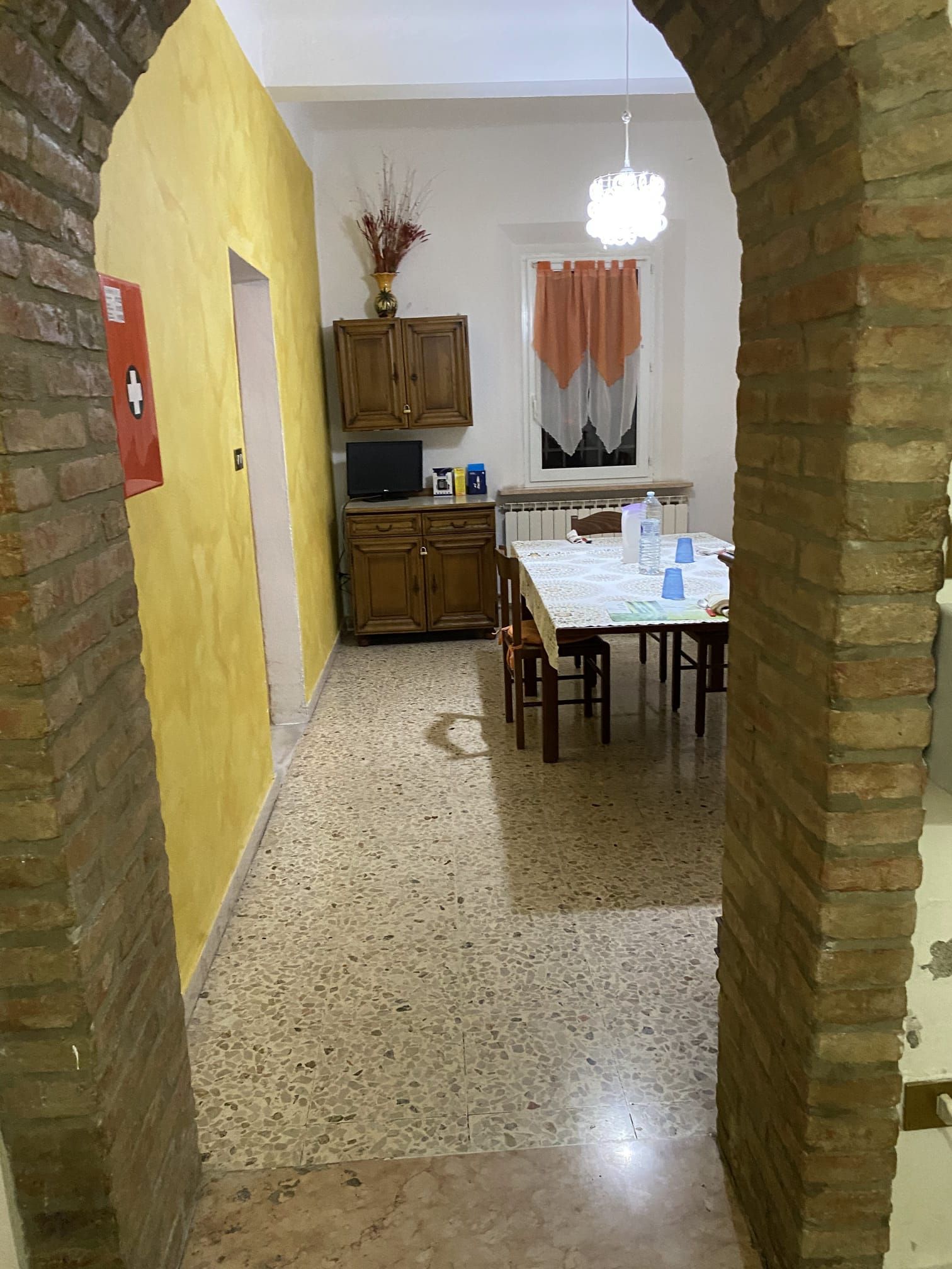 Un portale ad arco conduce alla sala da pranzo con tavolo, sedie e una credenza. Pareti e mattoni gialli.