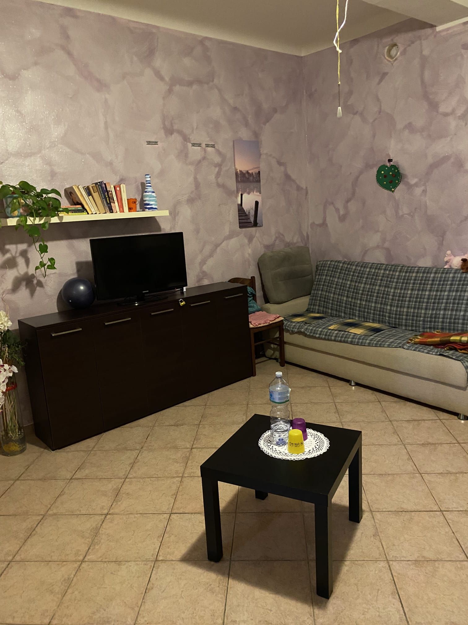 Soggiorno con mobili in legno scuro, pareti con motivi lilla e un piccolo tavolo quadrato nero.