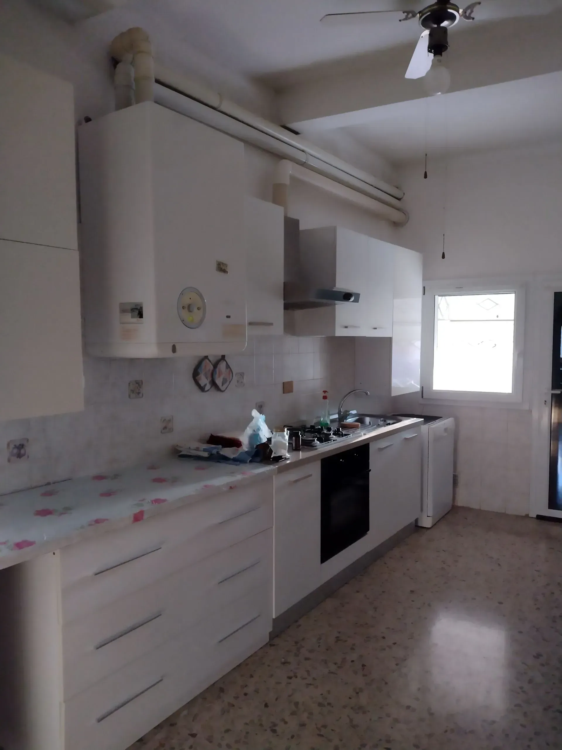 Cucina bianca con mobili, fornelli e finestra.