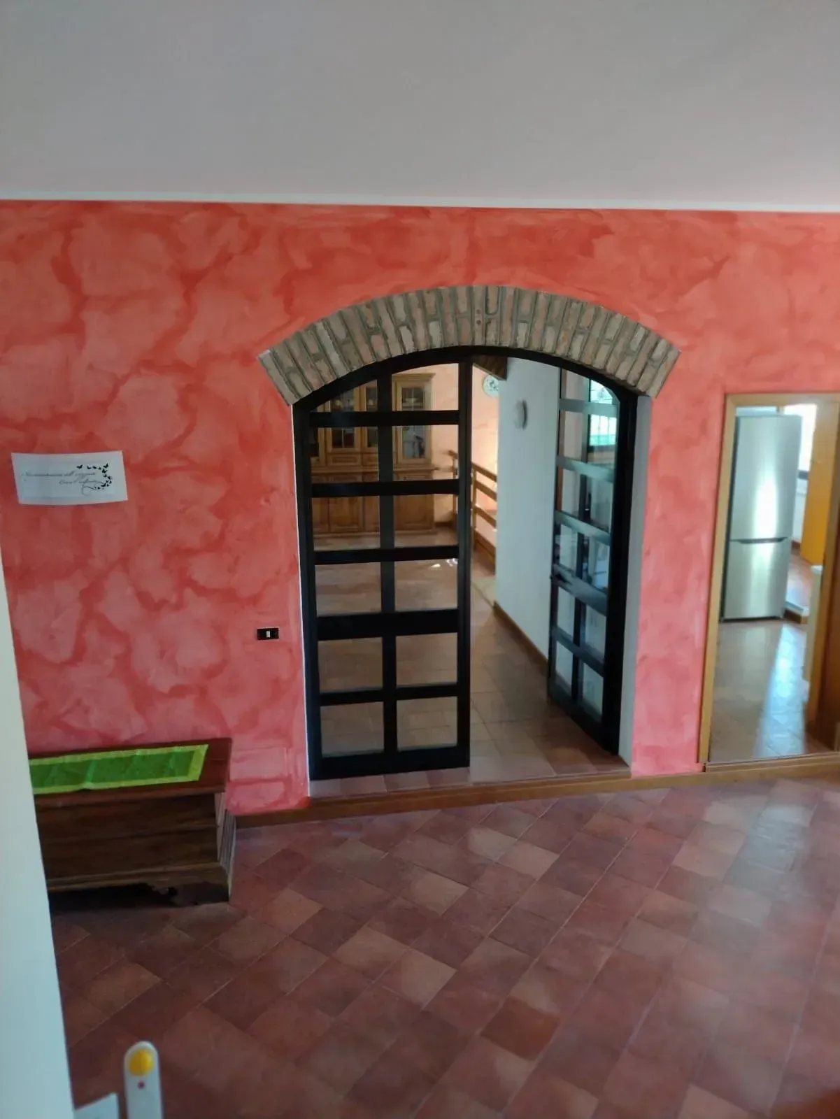 Stanza interna con pareti rosse testurizzate, porta ad arco con ante in vetro con cornice in metallo nero e pavimento piastrellato.