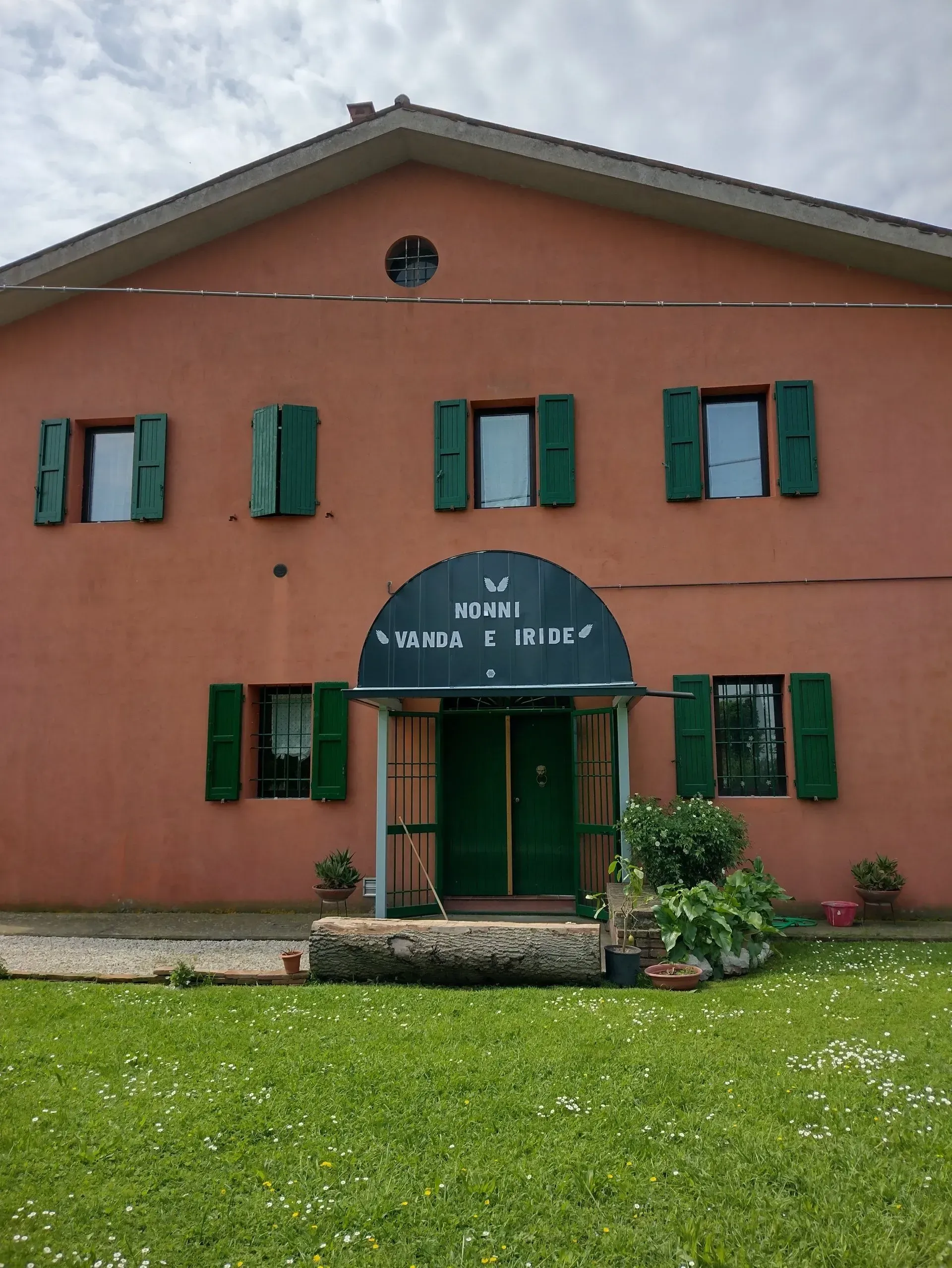 Edificio rosa con persiane e porta verdi, cartello con scritto 