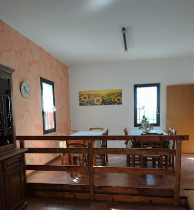 Zona pranzo con tavoli in legno, dipinto di girasoli e ringhiera in legno.