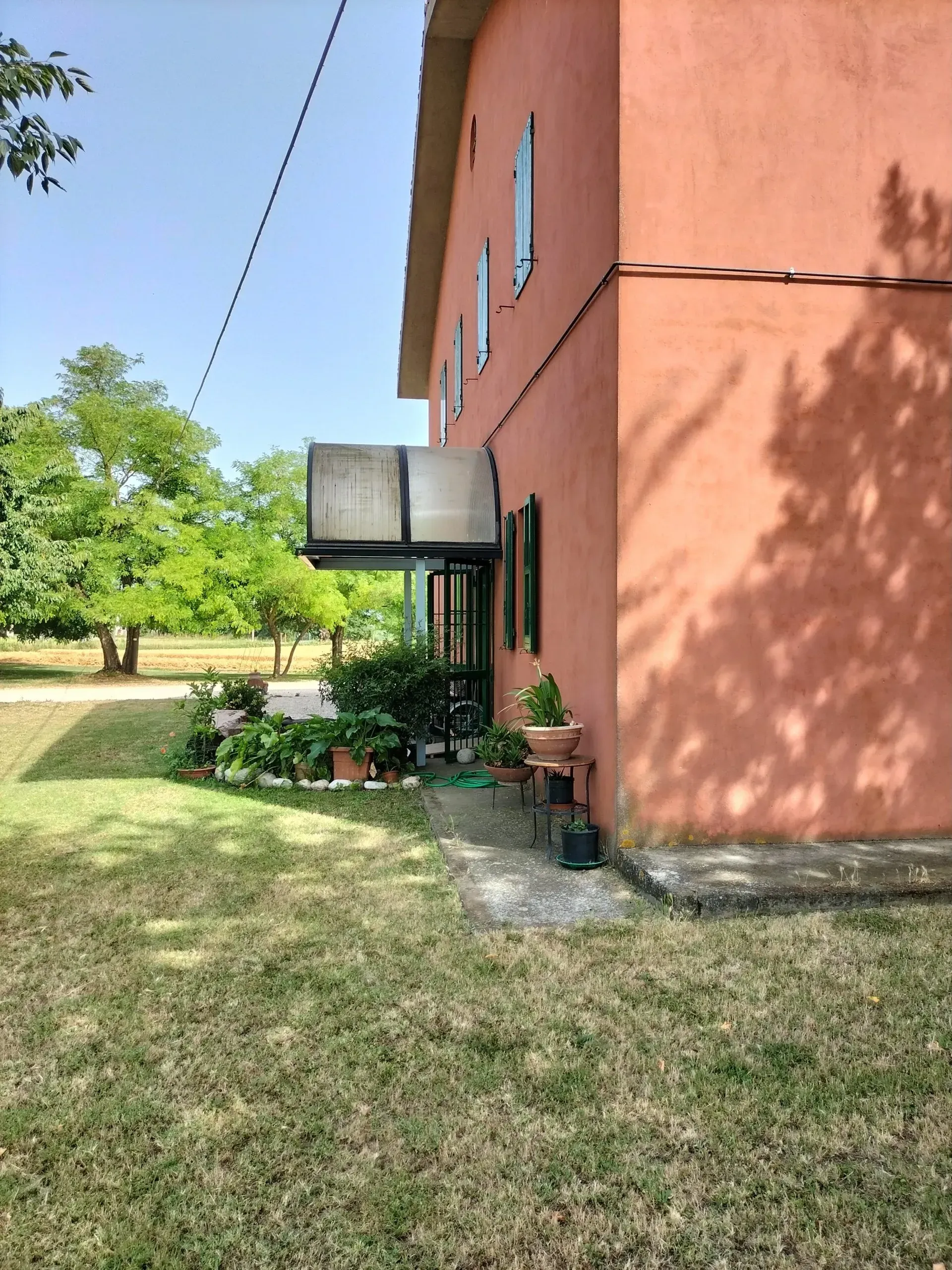 Edificio con pareti rosa, veranda coperta, piante e prato erboso sotto un cielo soleggiato.
