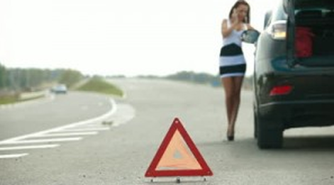 A woman is standing next to a warning triangle on the side of the road.