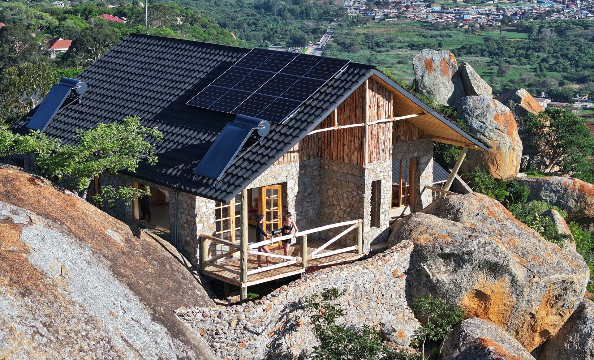 Stone cottage on a rocky hillside with solar panels on the roof and a wooden porch overlooking a scenic view.