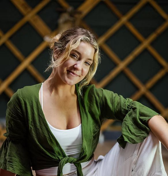 A woman in a green top and white pants is smiling
