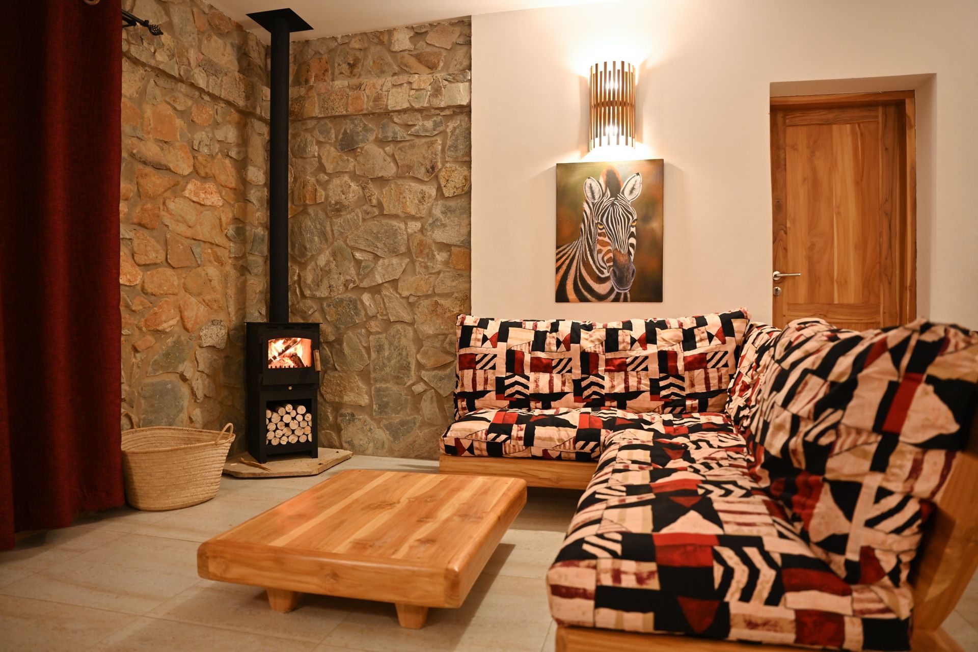 Cozy living room with stone wall, wood stove, patterned sofa, wooden coffee table, and zebra painting.