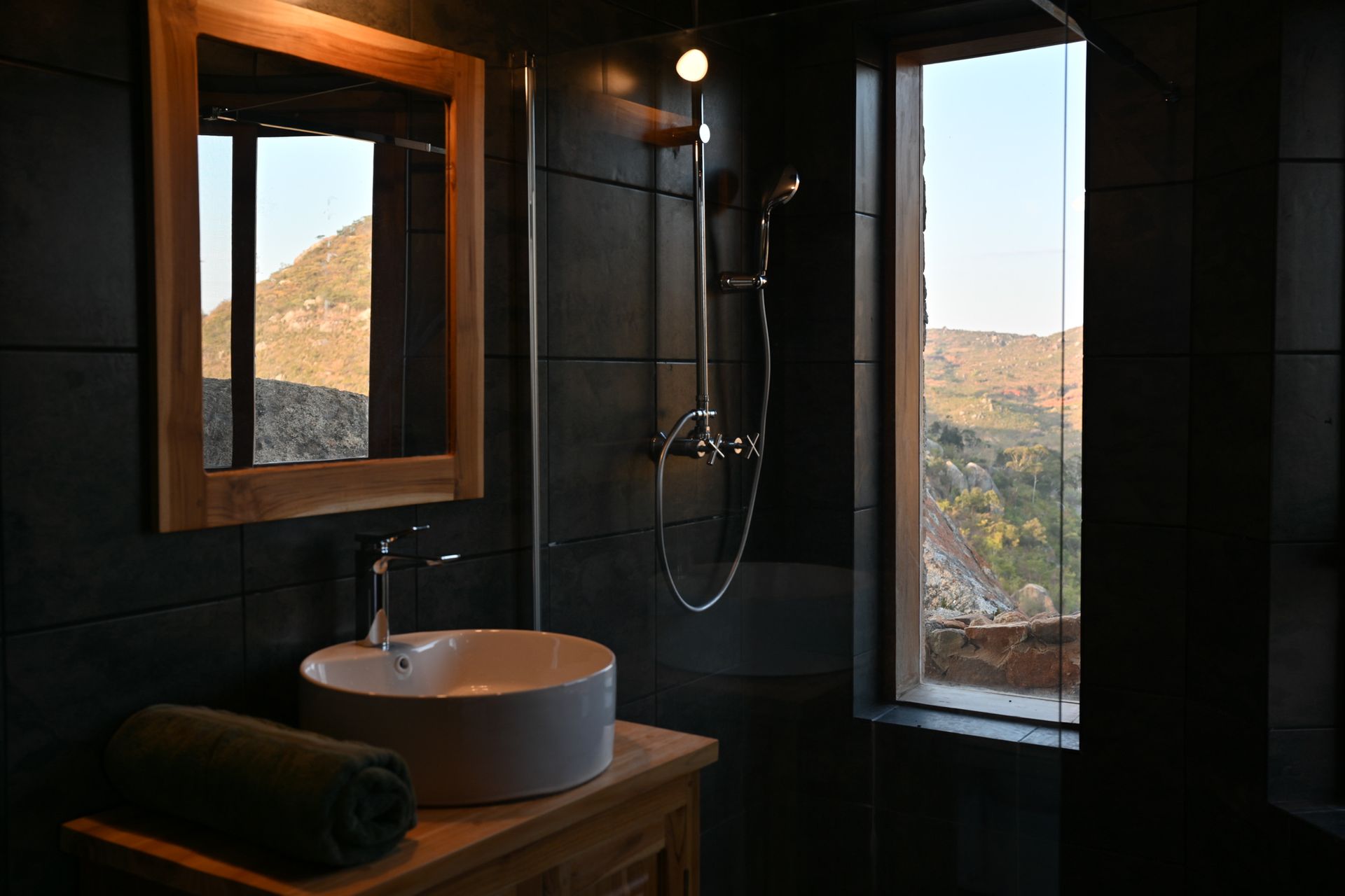 Bathroom with dark gray tiles, wooden vanity, and large window with outdoor view.