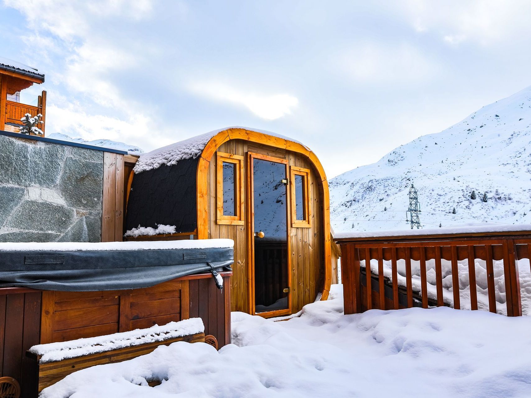 A wooden sauna is sitting in the snow next to a hot tub.
