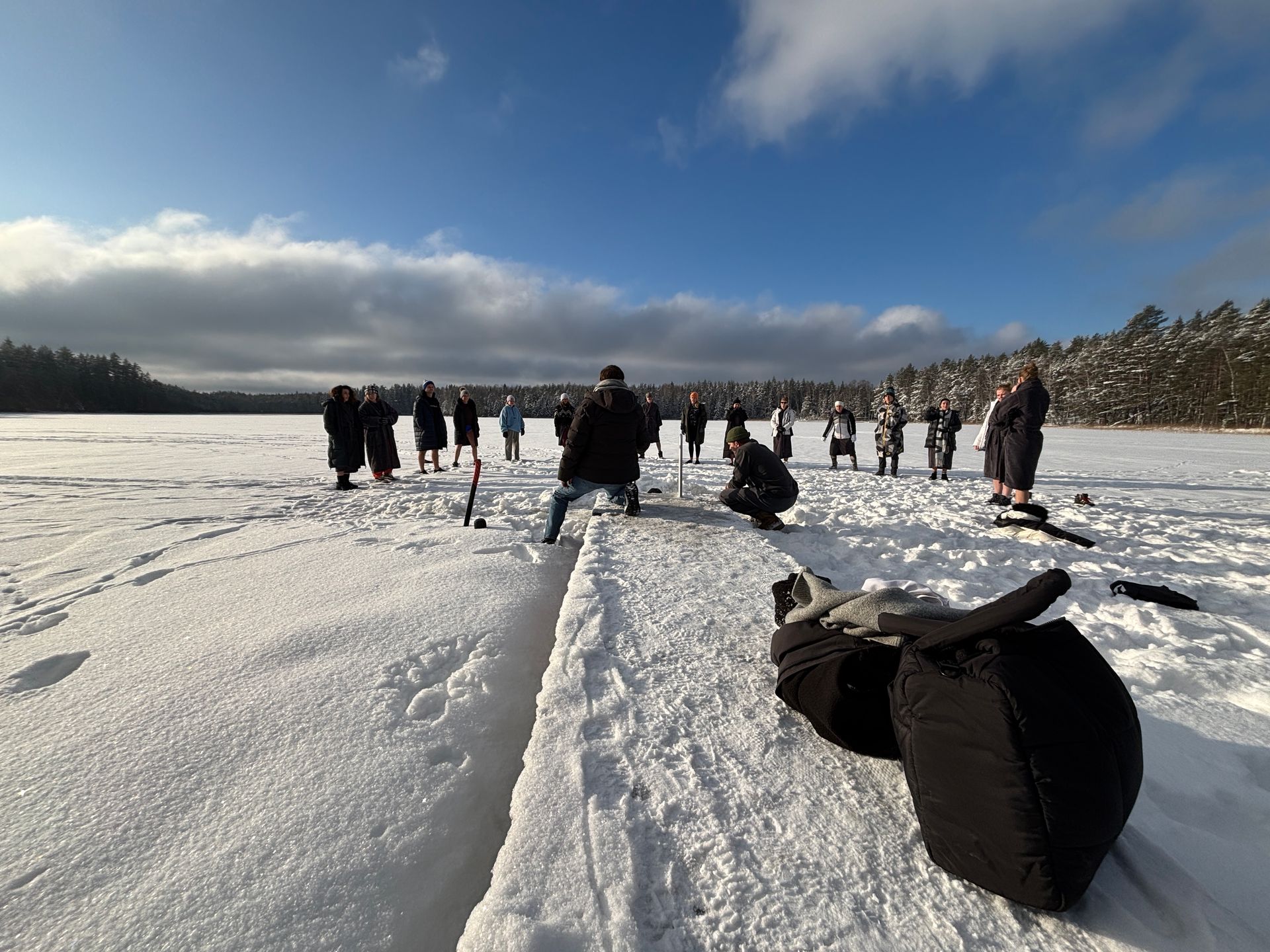 People preparing to enter a hole in the ice on a snow-covered lake, bright blue sky, sunny.