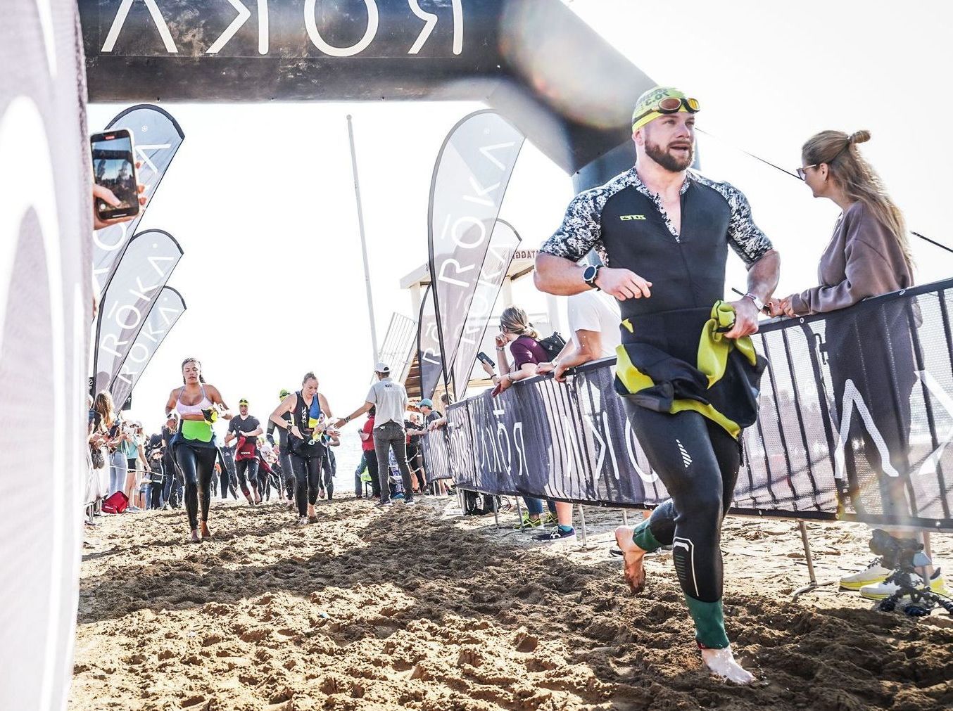 A man in a wet suit is running across a sandy beach.