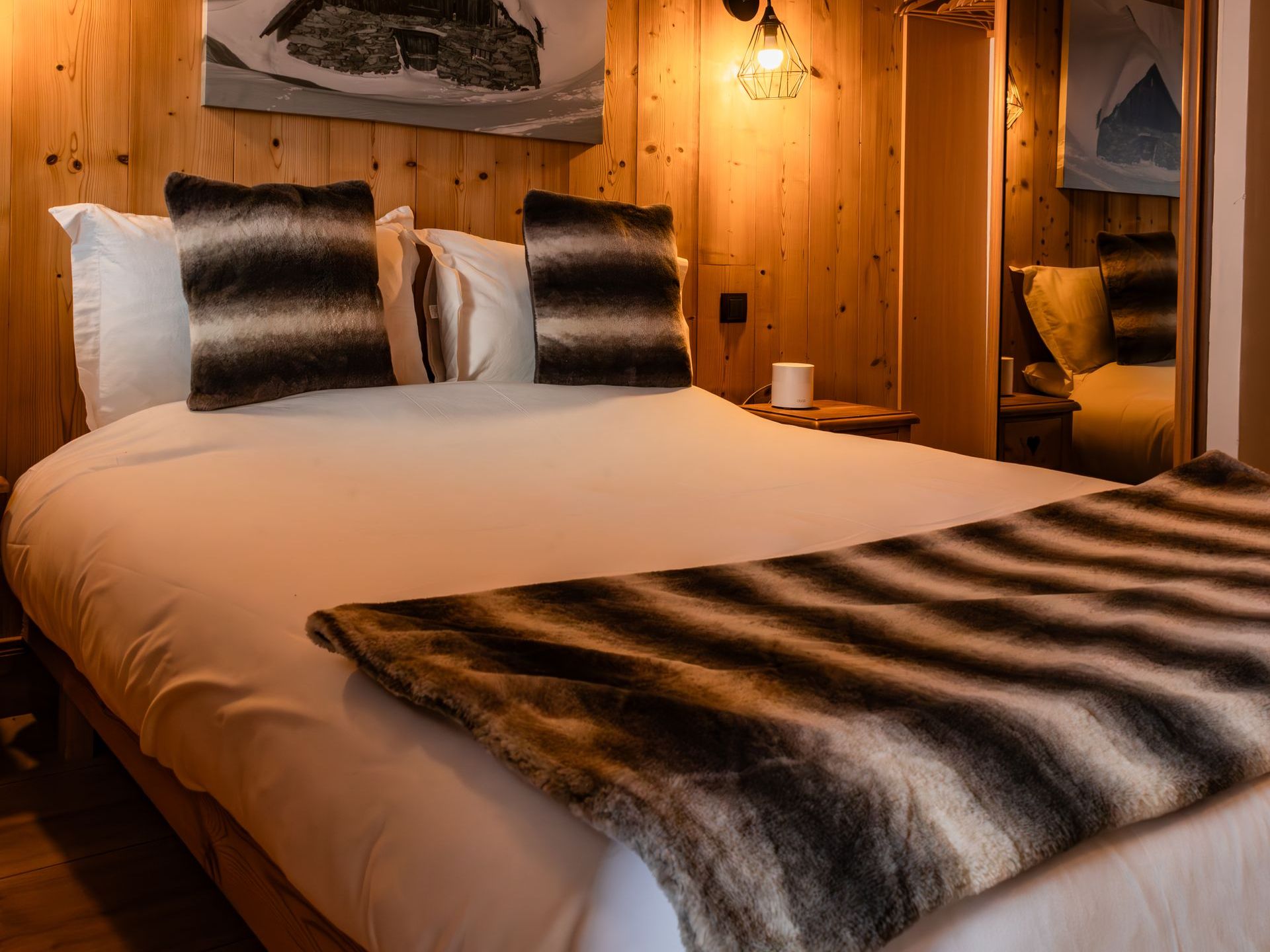 A bedroom with a bed , pillows , a blanket and a mirror.