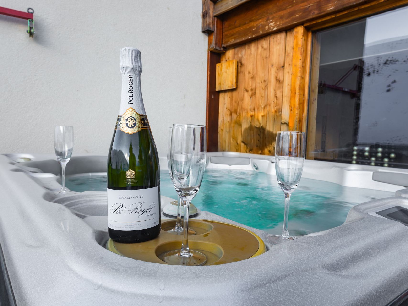 A bottle of champagne and two glasses are sitting on top of a hot tub.