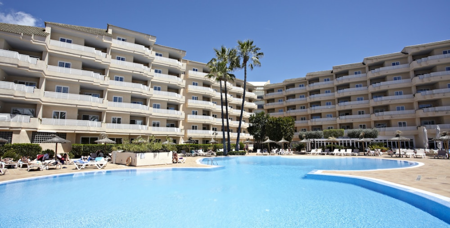 Large resort pool with turquoise water surrounded by sunbathers, lounge chairs