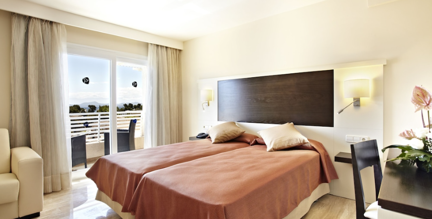 Hotel room with two beds, balcony view, beige and brown decor, flowers.