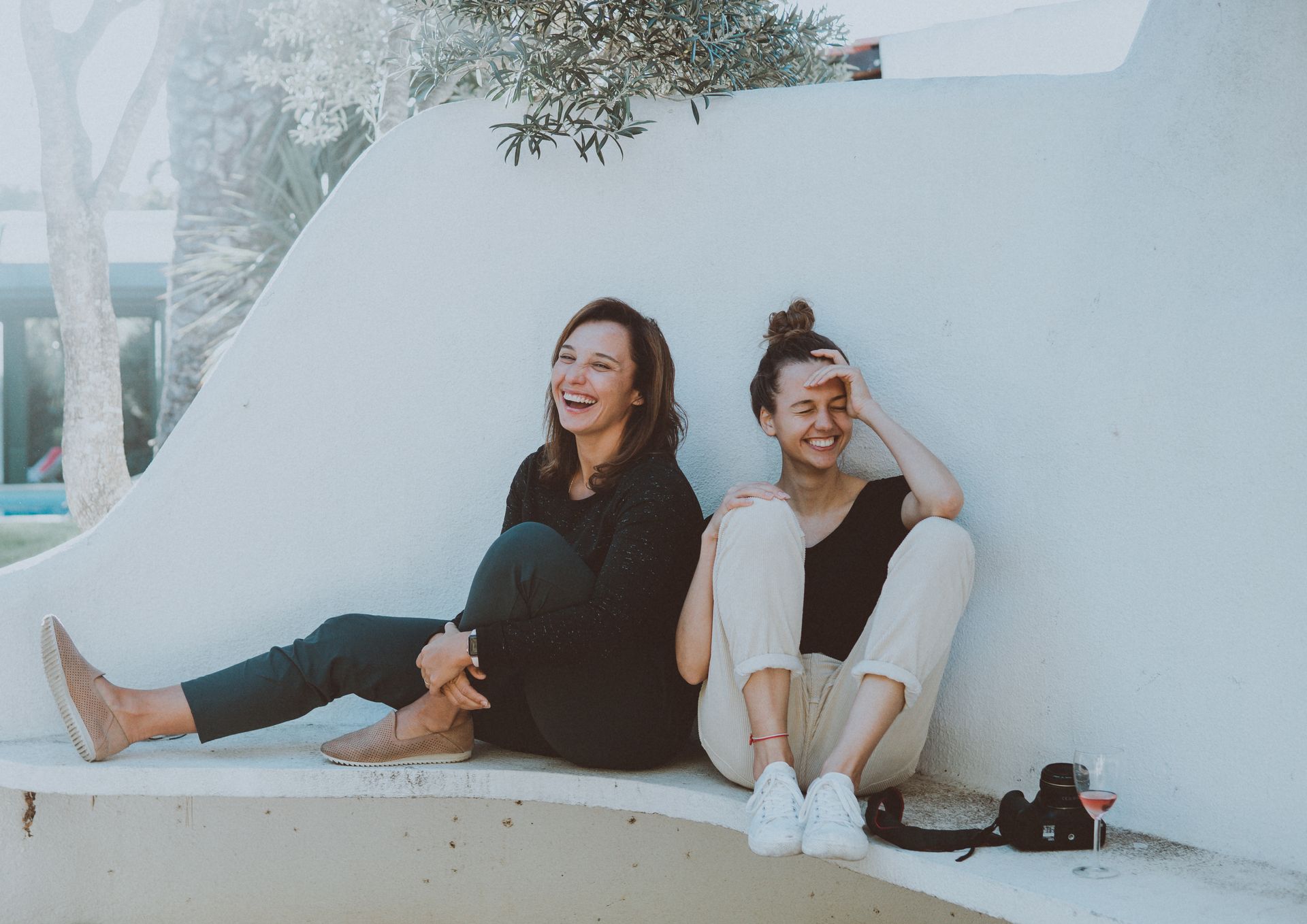 Two women are sitting next to each other on a bench and laughing.