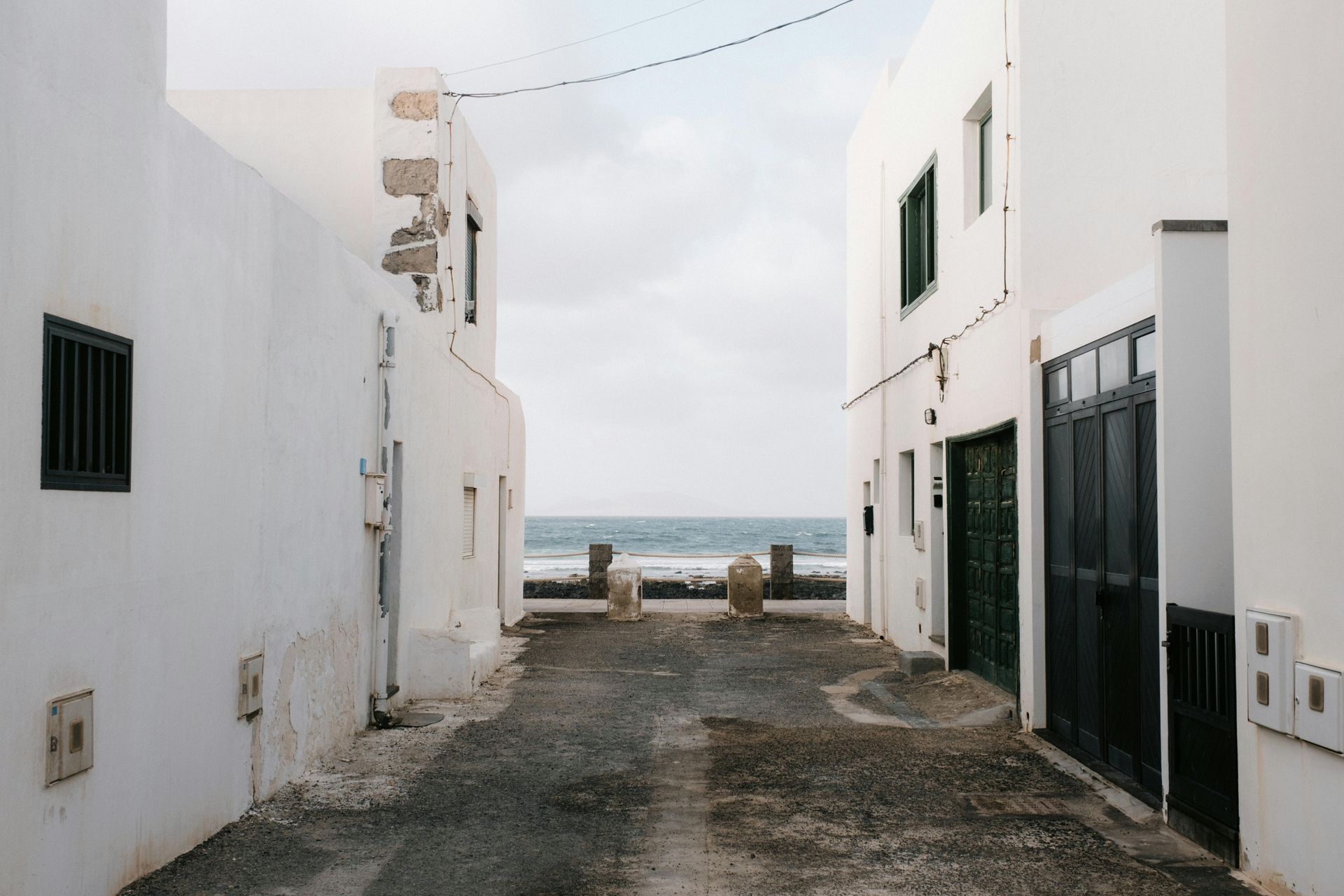 A narrow alleyway between two white buildings with a view of the ocean.