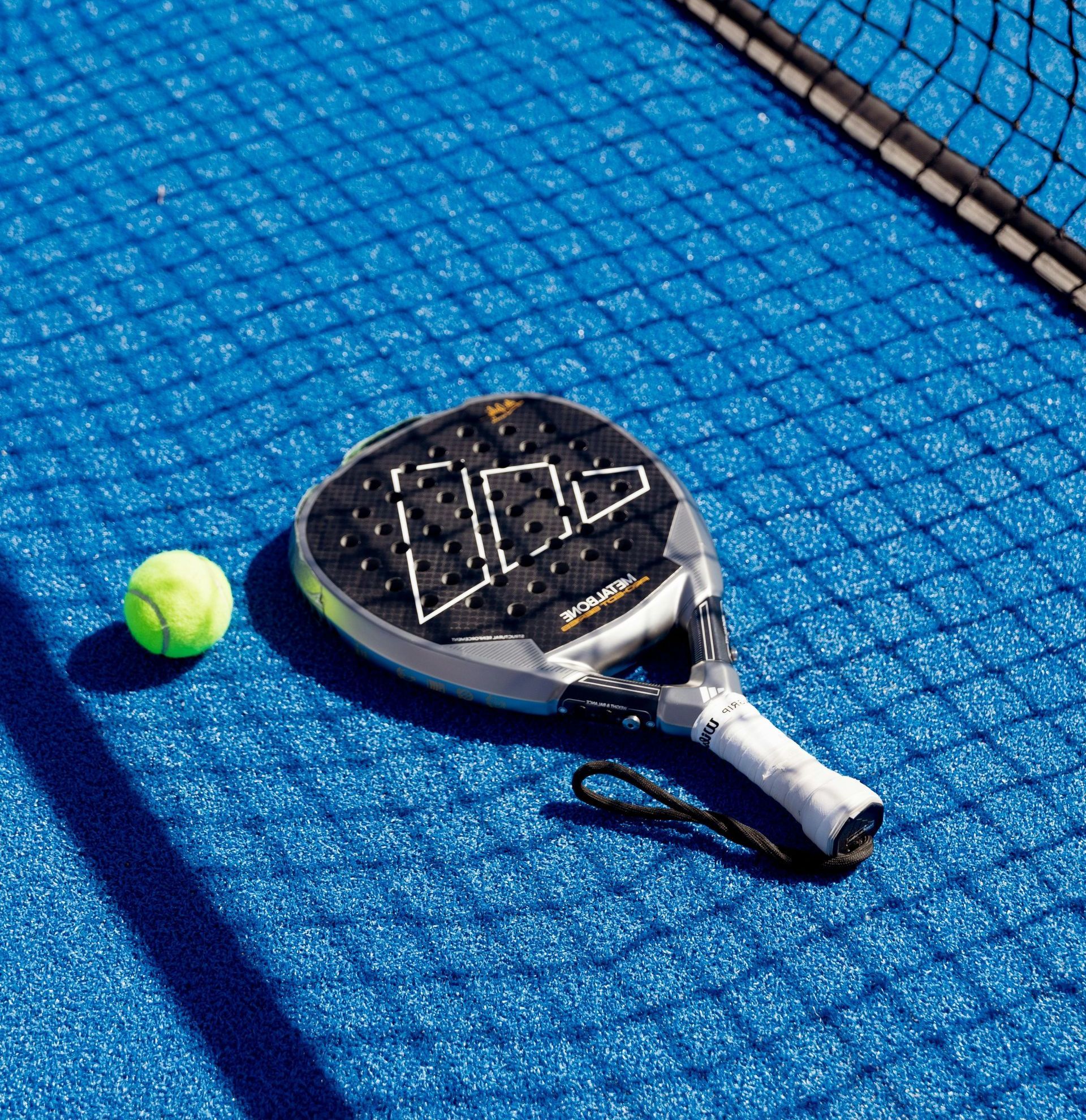 A padel racket and ball are on a blue tennis court.