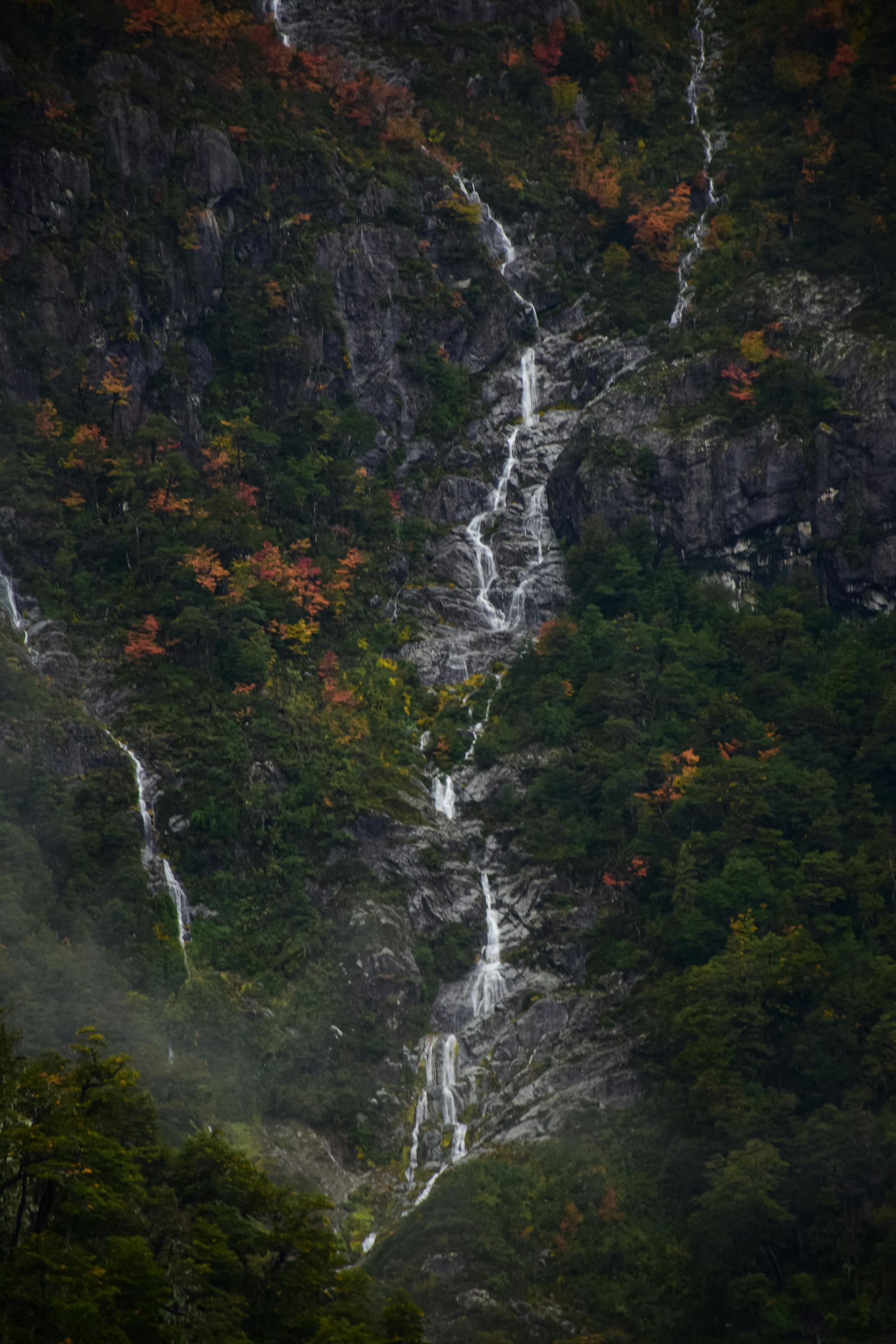 A waterfall is coming down the side of a mountain surrounded by trees.