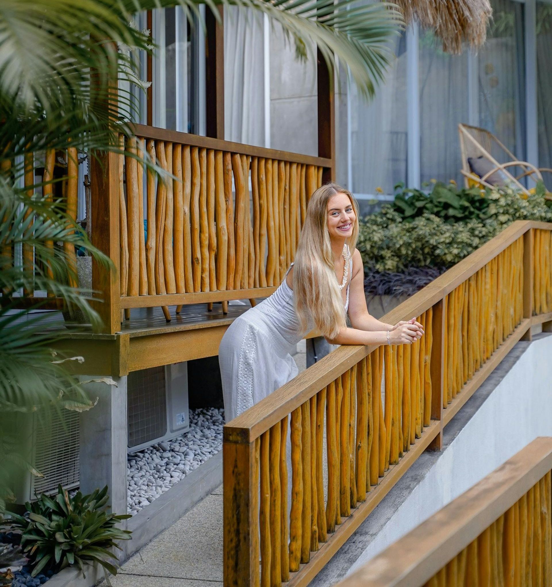 A woman in a white dress is leaning on a wooden railing.