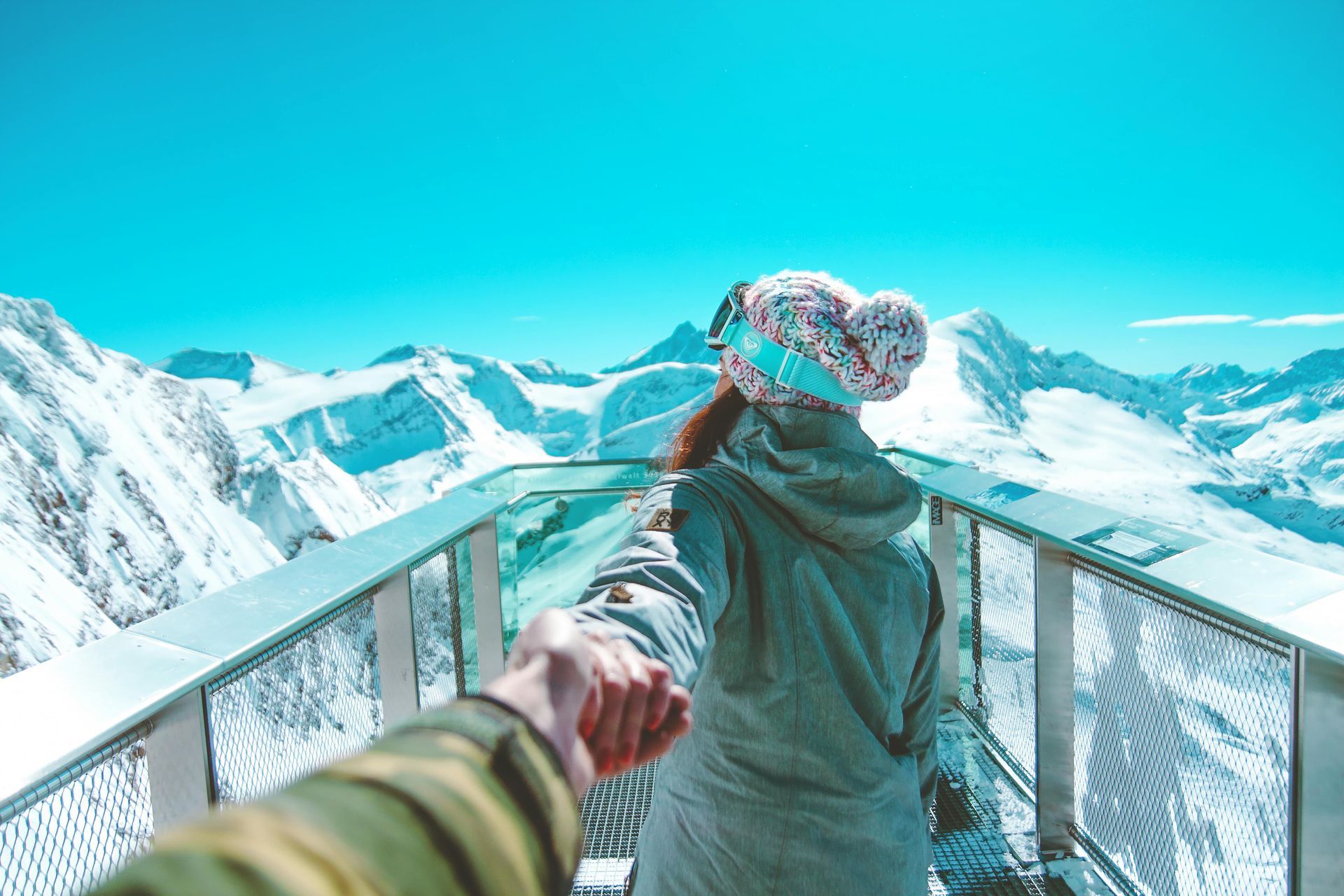 A man is holding a woman 's hand while standing on a balcony overlooking snow covered mountains.