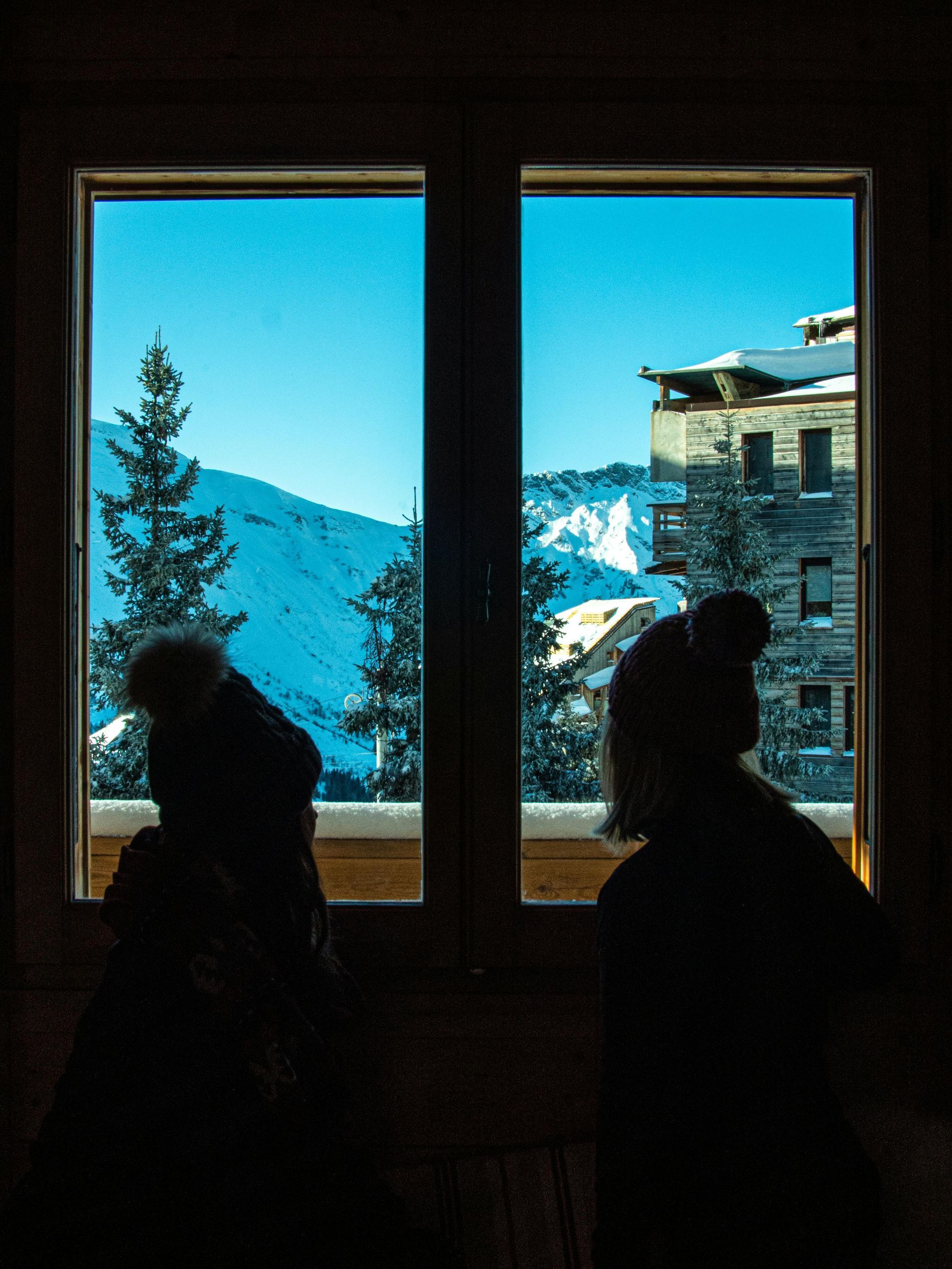 Two people are looking out of a window at a snowy mountain.