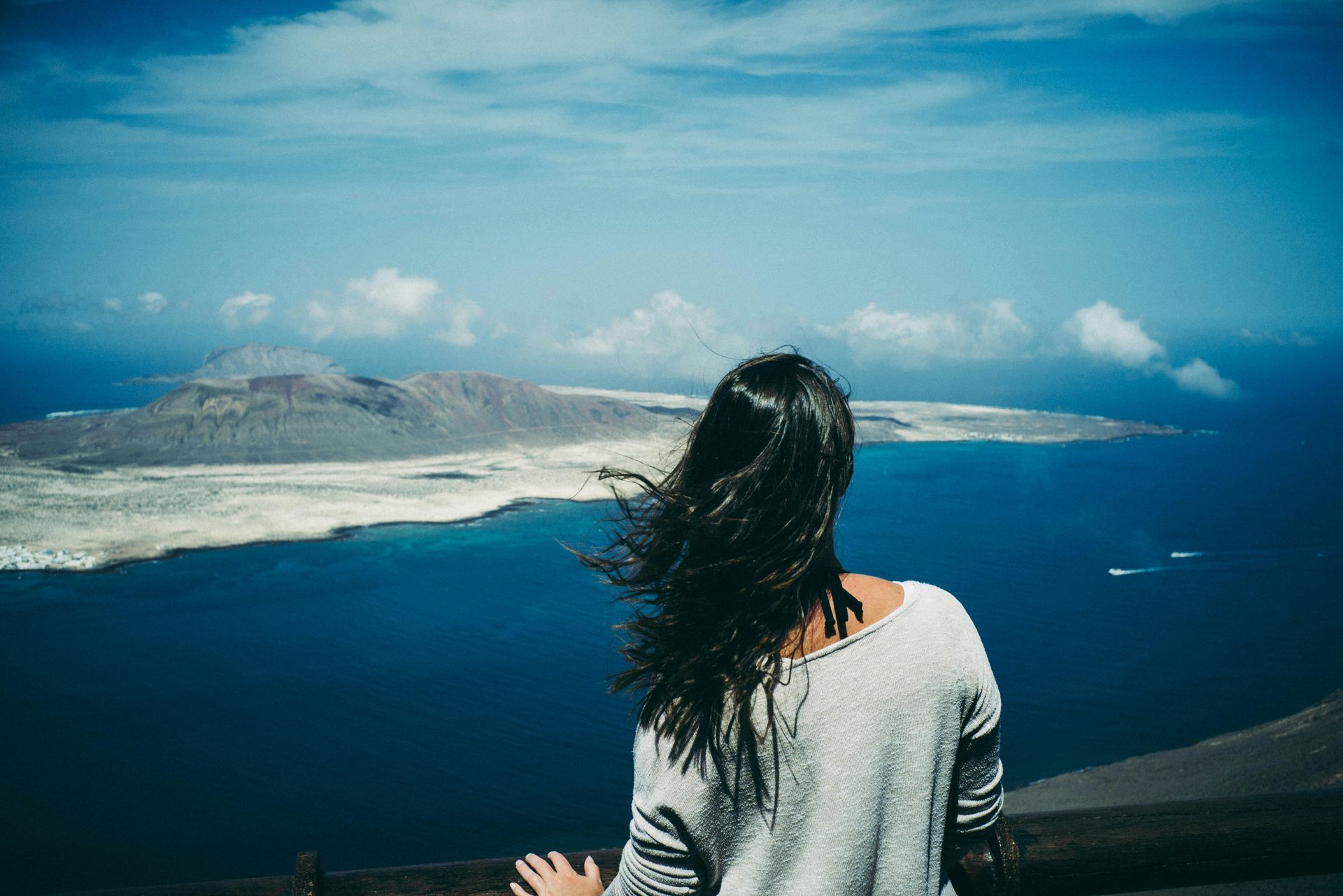 A woman is standing on top of a hill overlooking the ocean.