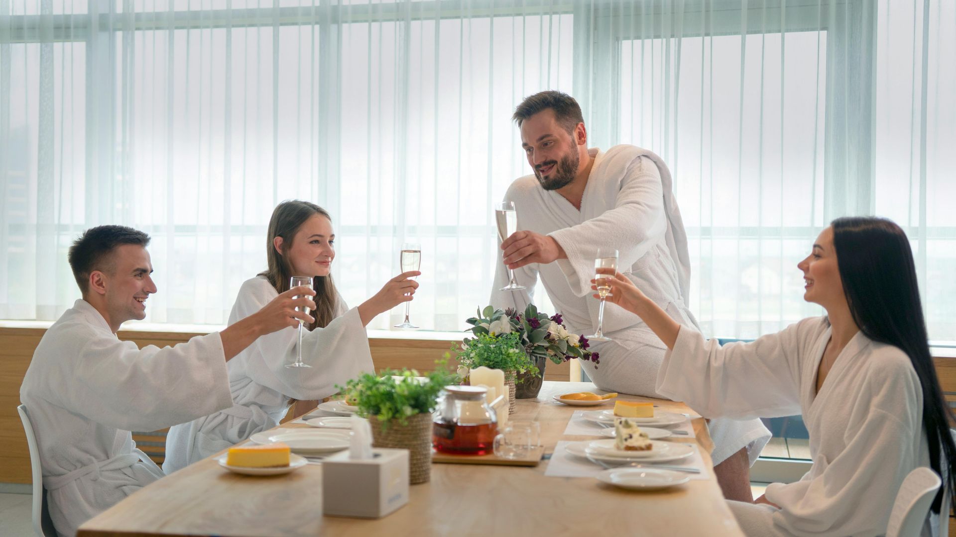 A group of people in bathrobes are sitting at a table toasting with champagne.