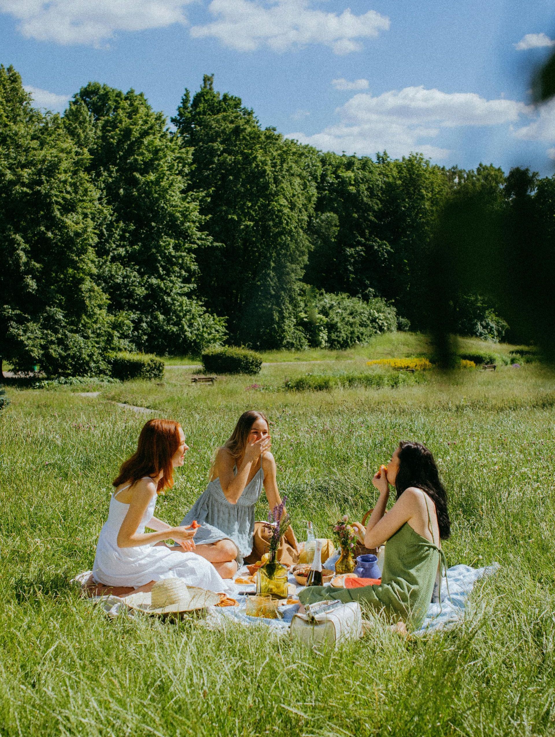 Three women are having a picnic in the grass in a park.