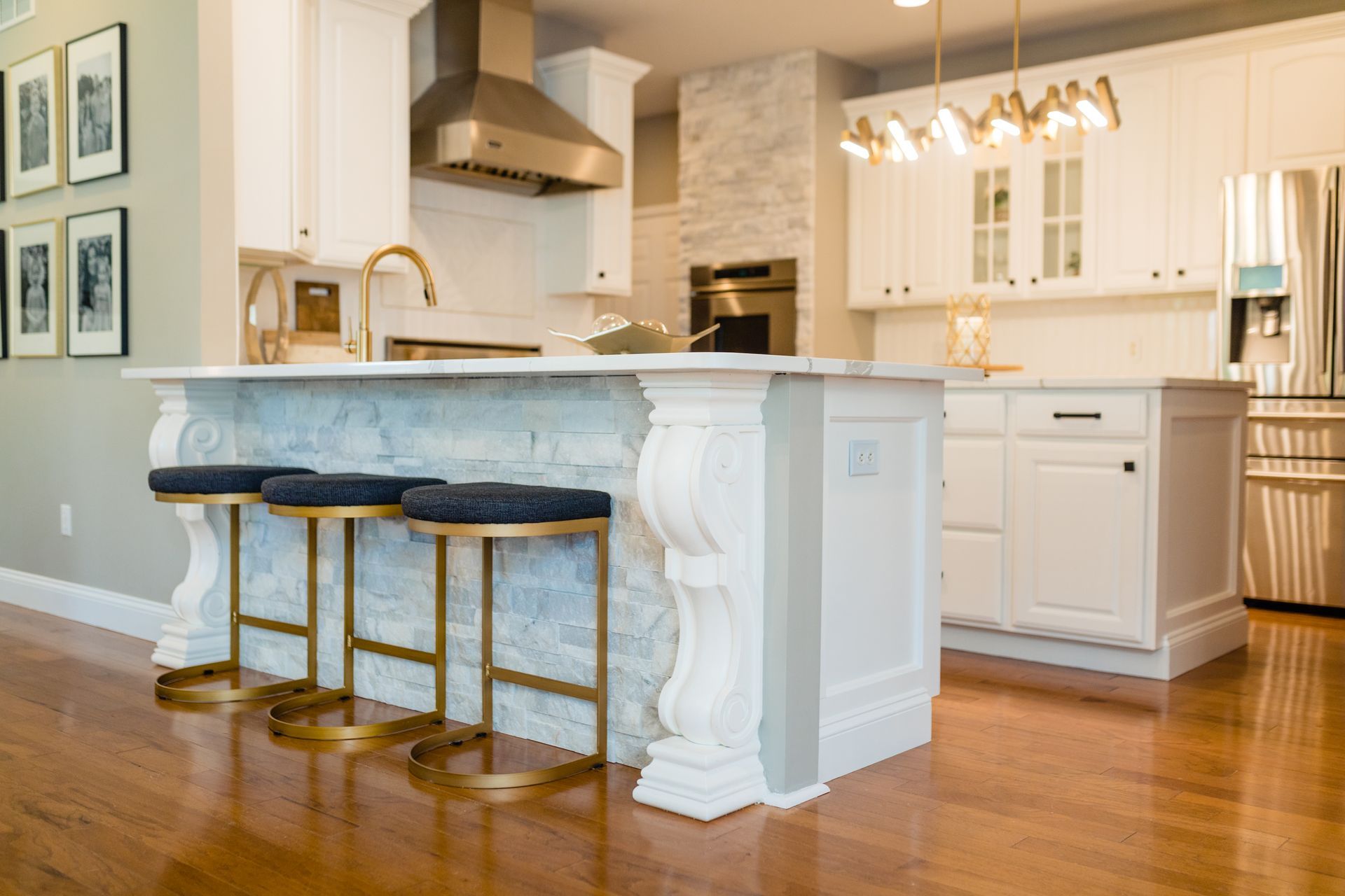 A kitchen with white cabinets , wooden floors , stools and a large island.