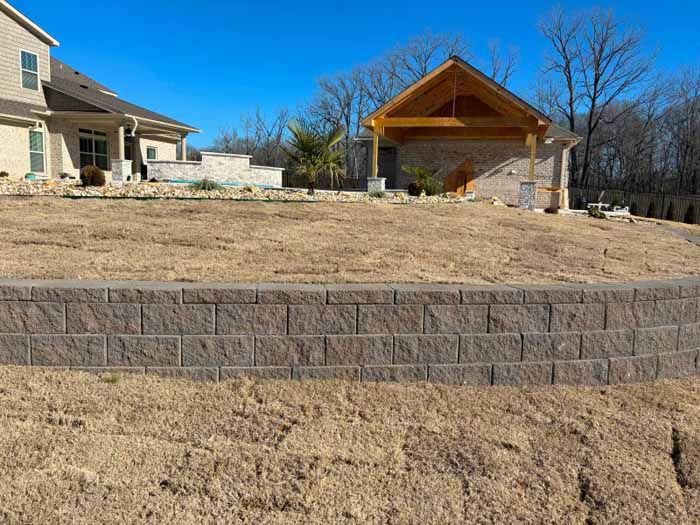 There is a brick wall in the middle of a field in front of a house.