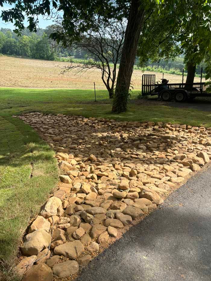 A driveway with rocks on the side of it and a field in the background.