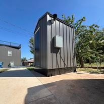 A small shed is sitting in the middle of a driveway next to a building.