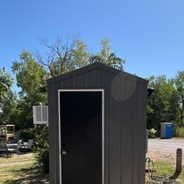 A small shed with a black door is sitting in the middle of a field.