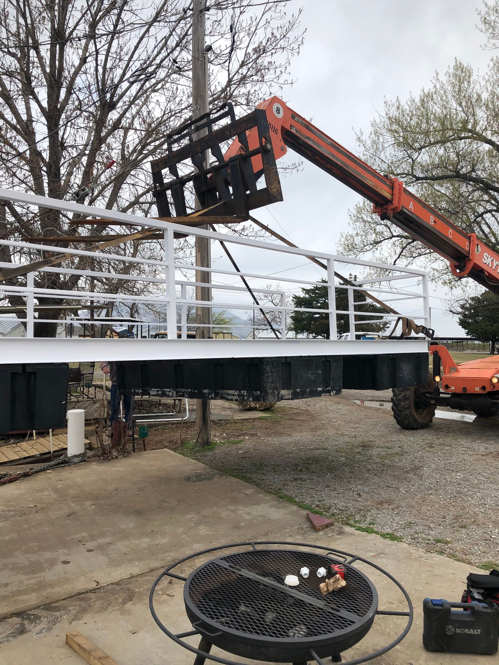 A crane is lifting a railing over a fire pit.