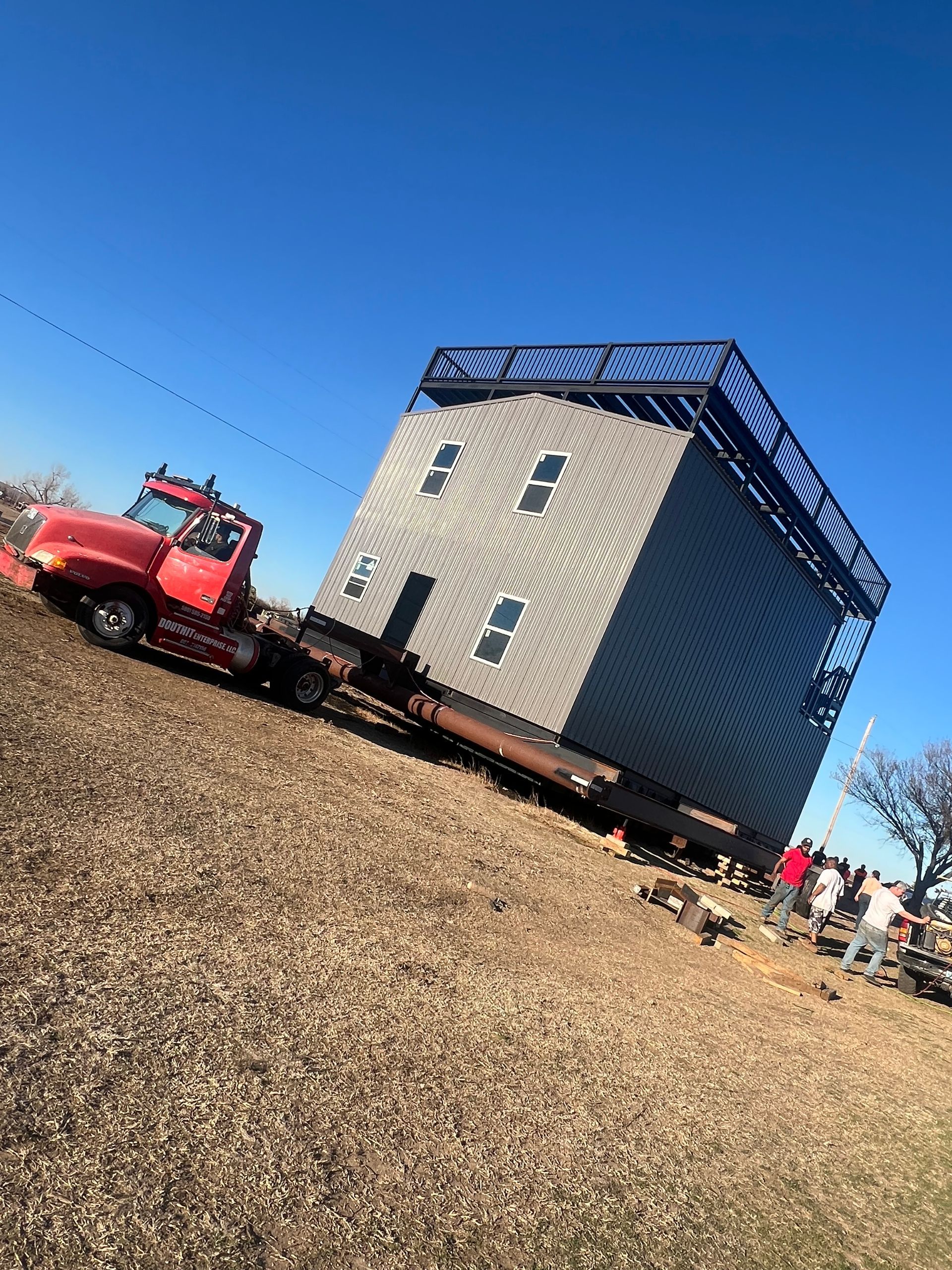 A large house is being towed by a tow truck in a field.