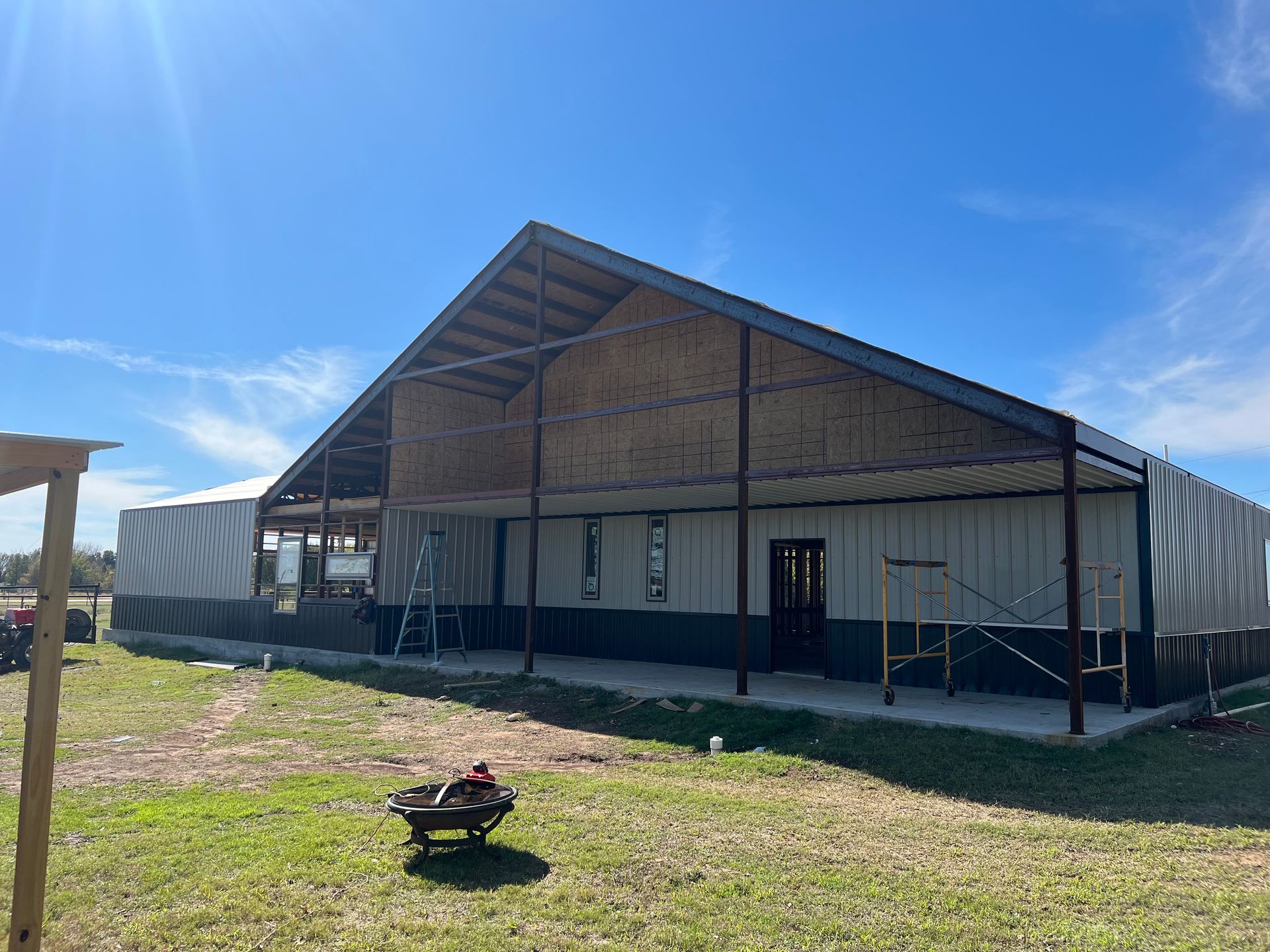 A large building is being built in a field with a wheelbarrow in front of it.