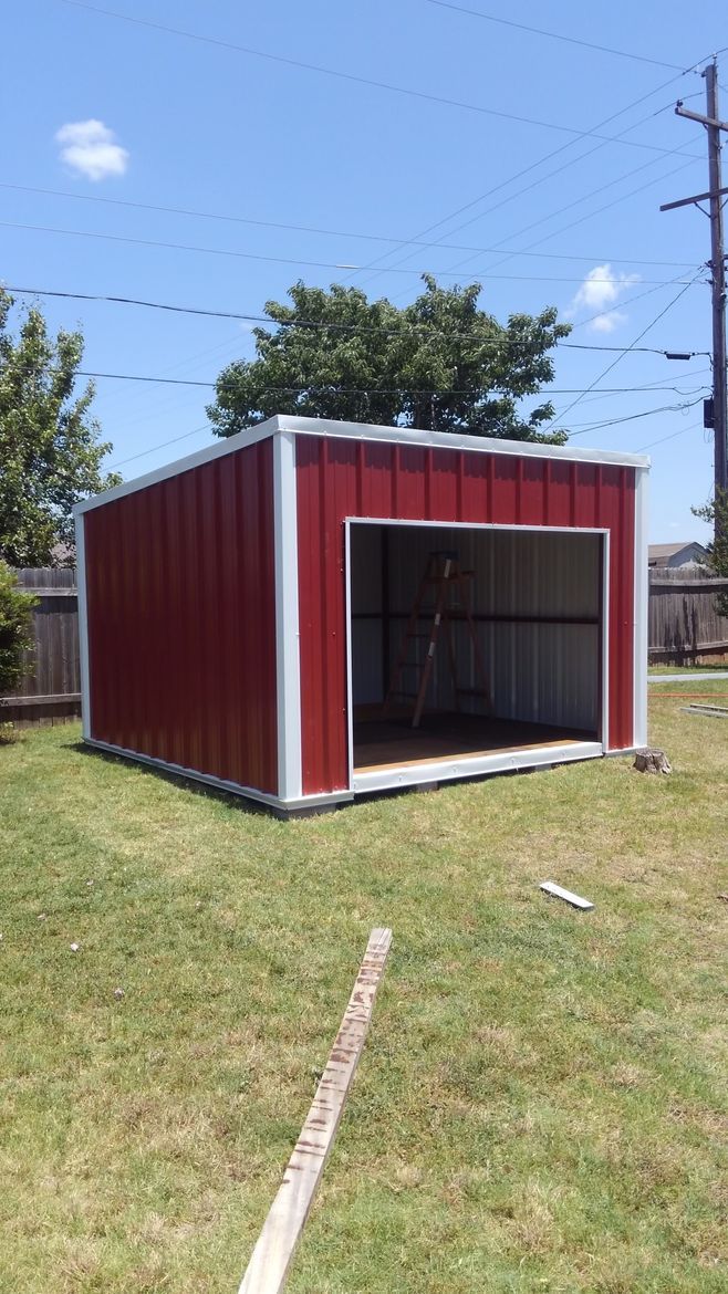 A red and white garage is sitting in the middle of a lush green field.