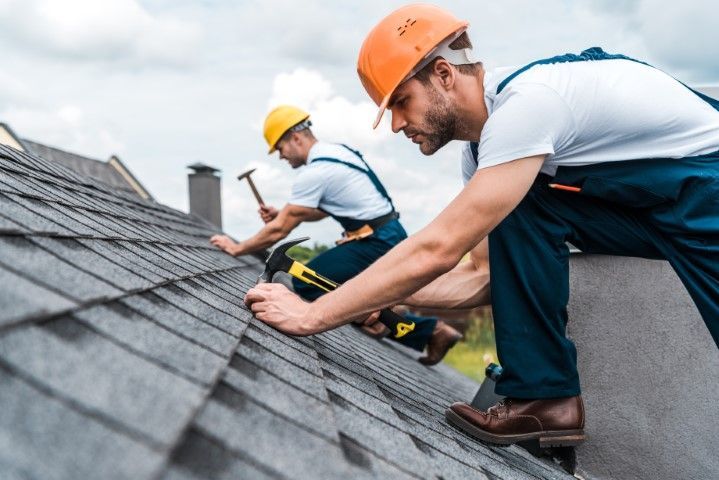 Two roofers wearing hard hats, installing shingles on a house roof.